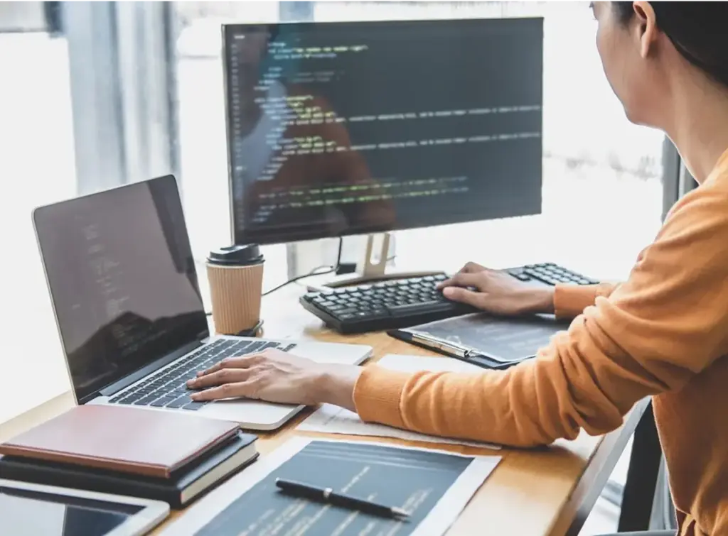 Person sitting at desk with one hand on laptop keyword and their other hand on desktop keyboard