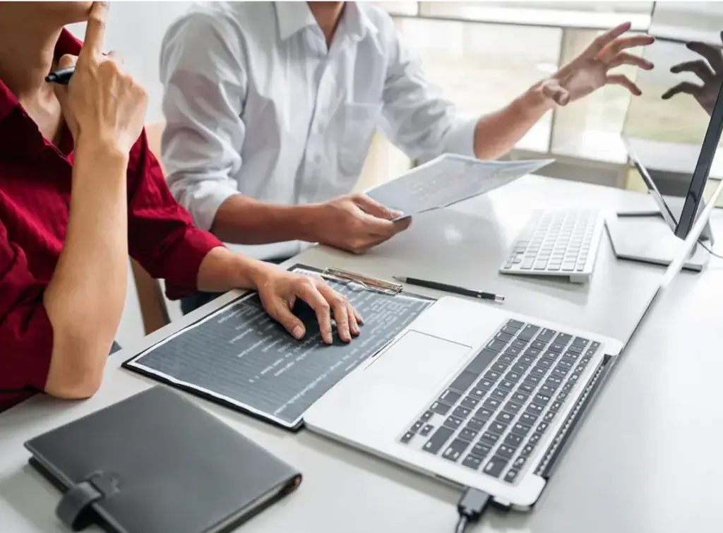 Clients sitting at desk with laptop, desktop, and clipboard